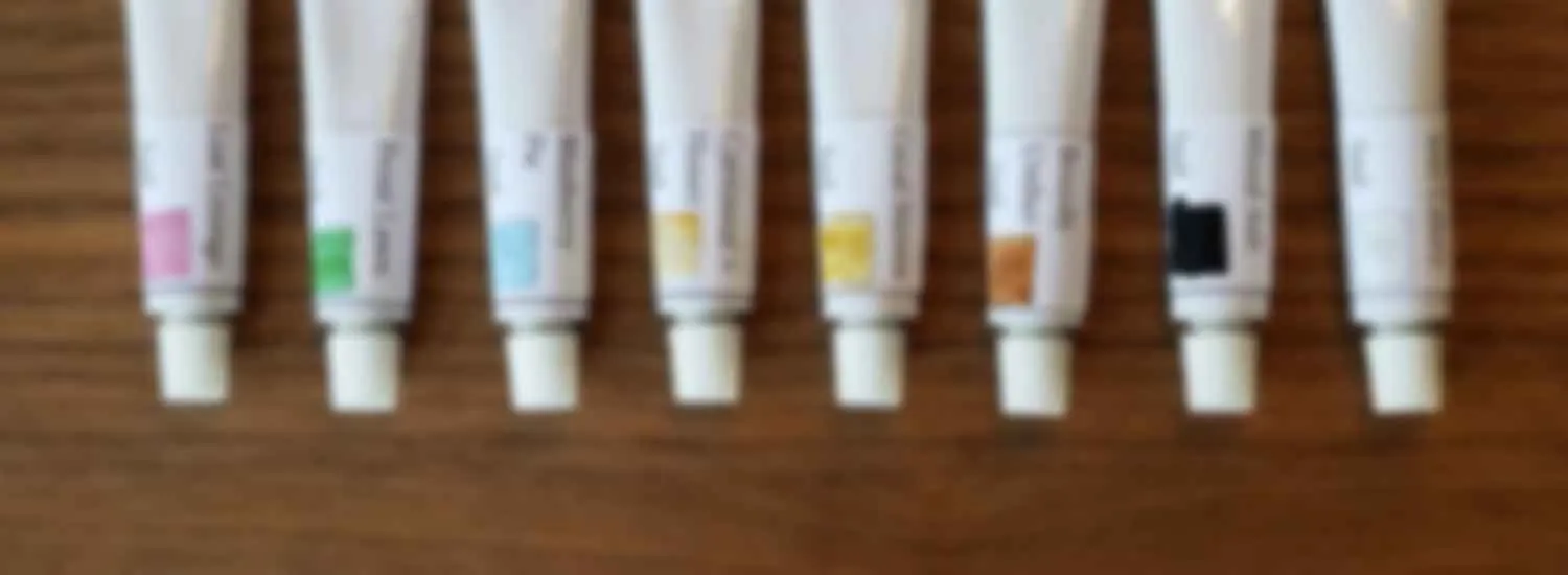 A row of watercolour paint tubes laid out on a wooden bench.